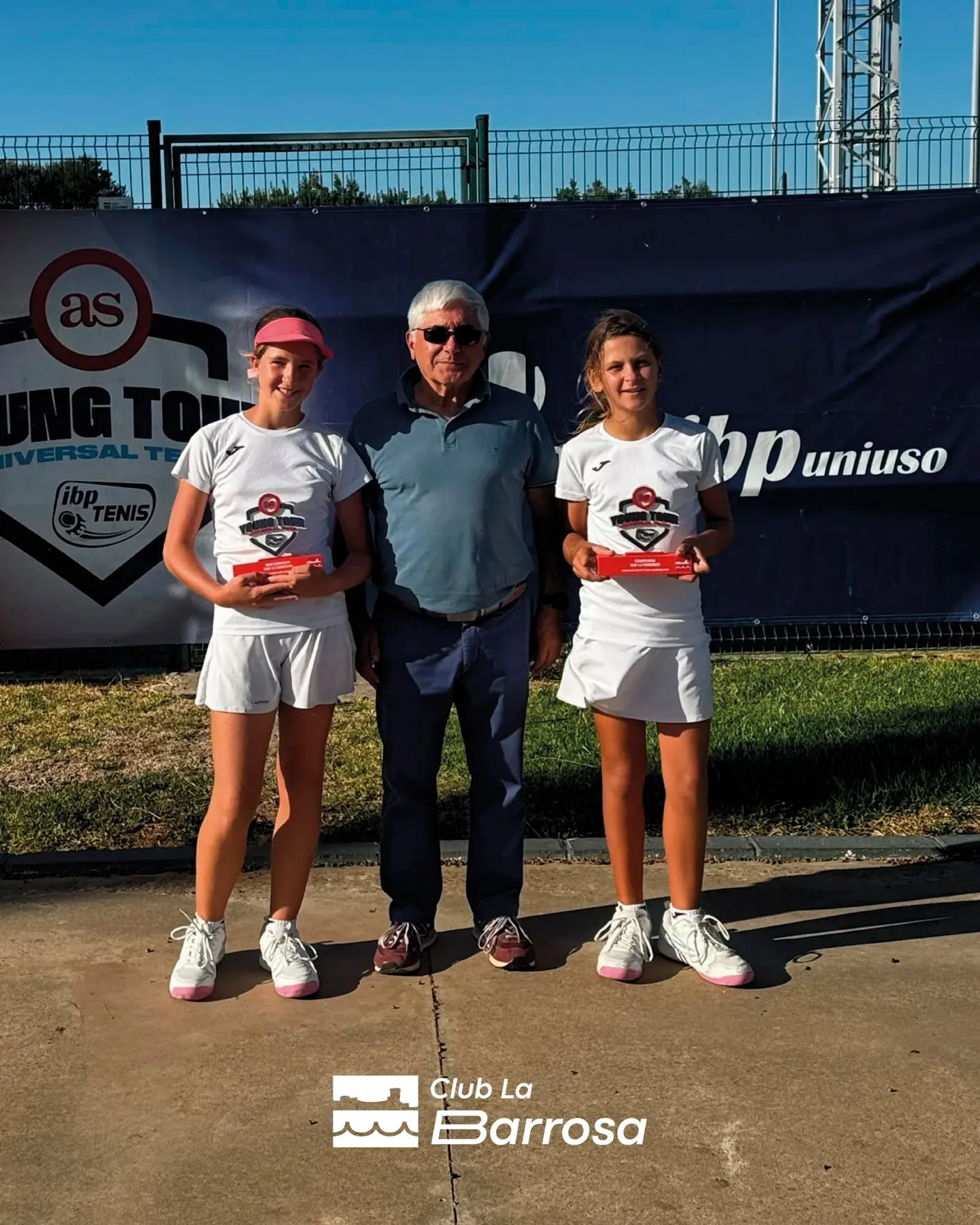 Jóvenes tenistas con sus trofeos y el vinilo del torneo de fondo