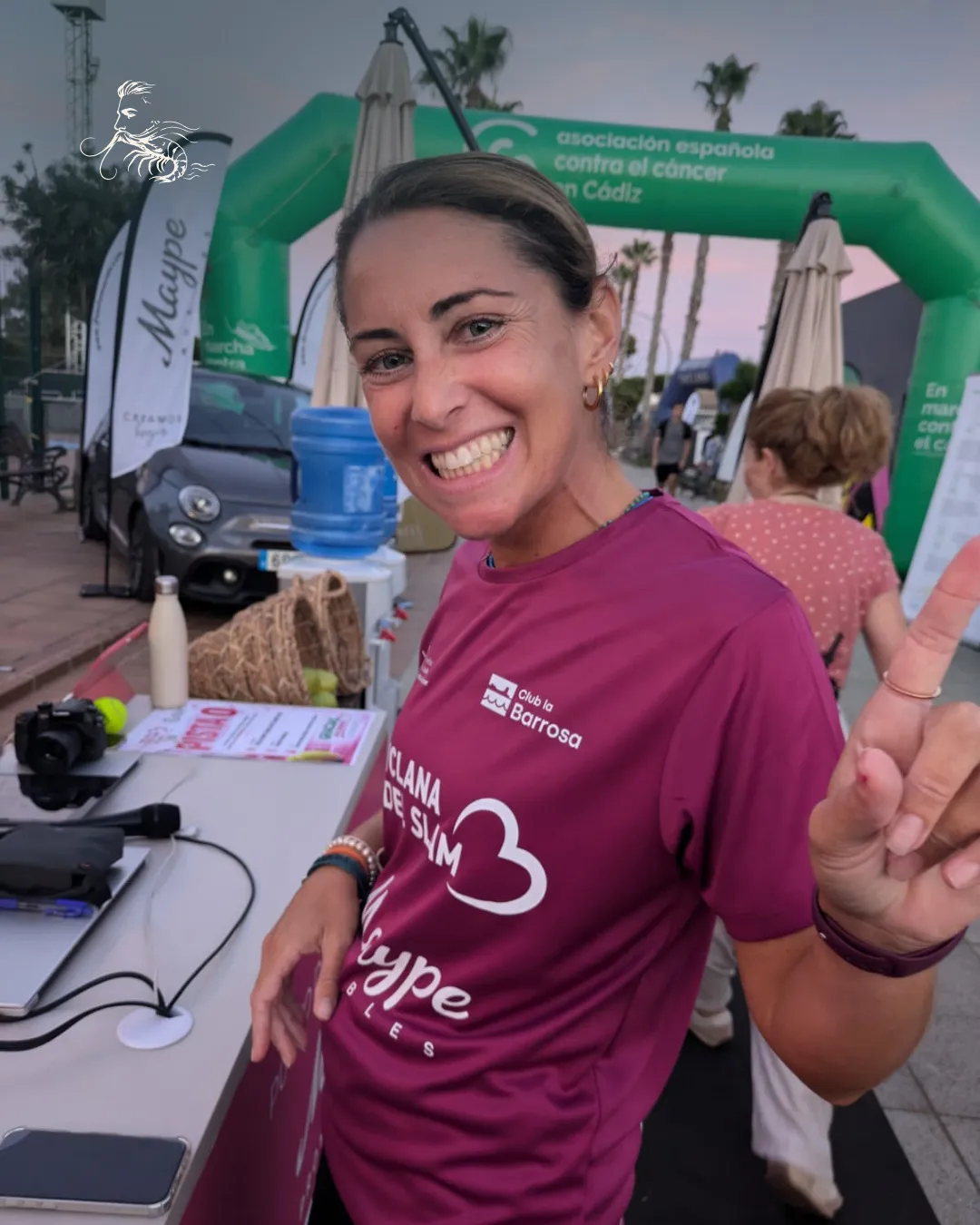 Jugadora con la camiseta del Chiclana Padel Slam y el arco de la Asociación Española Contra el Cáncer al fondo