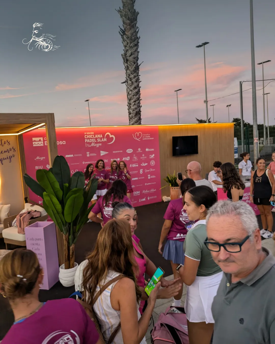 Público y jugadoras al atardecer frente al photocall del torneo en el Club La Barrosa